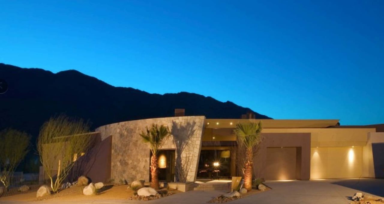 Modern stone-front home with desert landscaping and mountains behind it at dusk.