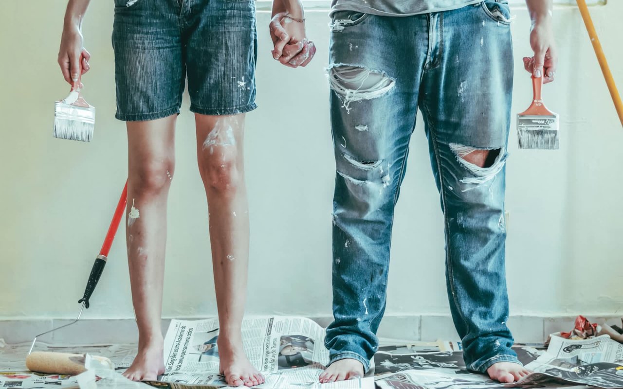  A pair of bare legs and feet stand on newspaper-covered floor, splattered with white paint. 