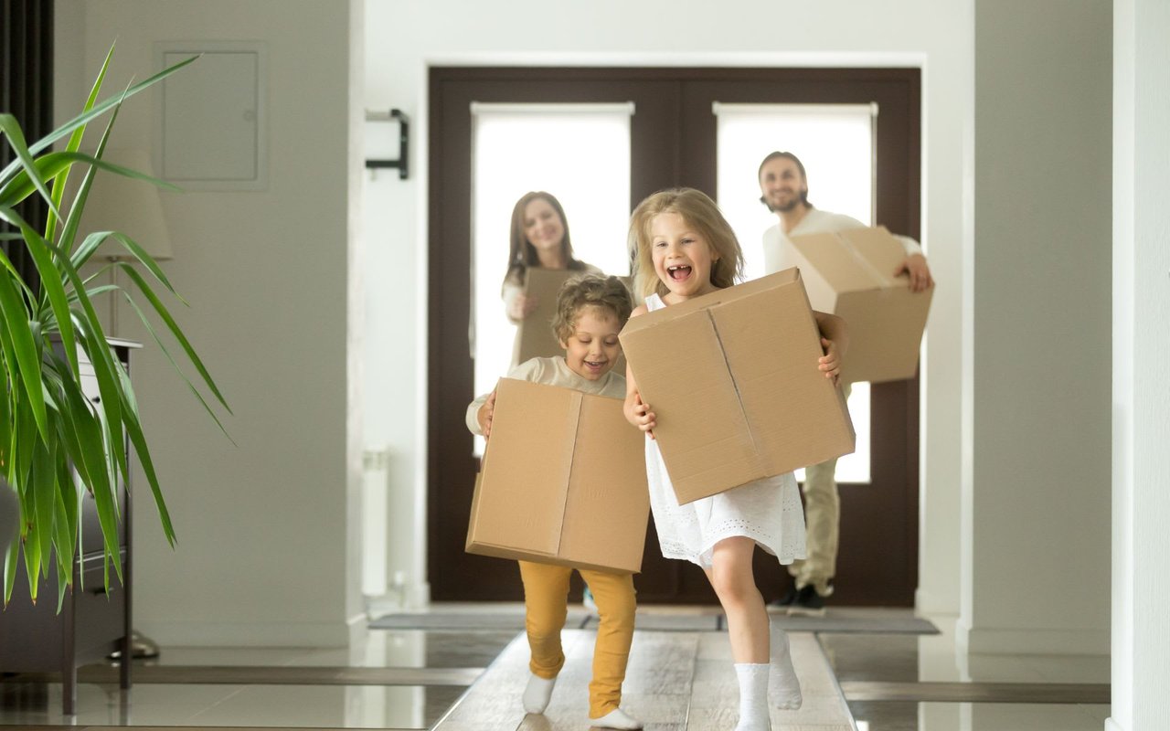 Move up versus second home. Which one is right for you. Two children with their parents running into a home with cardboard moving boxes