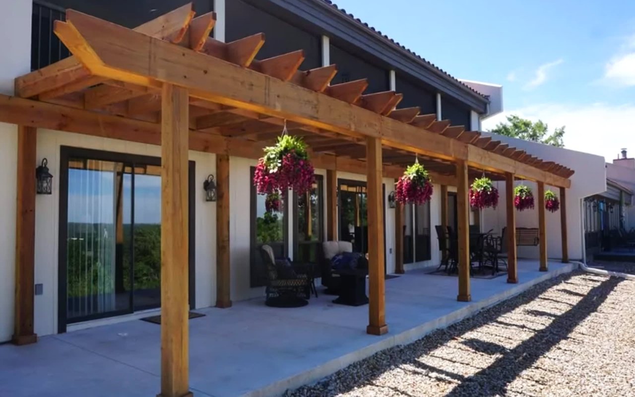  A wide, outdoor patio area extends along the side of a modern building with white walls and dark windows. 