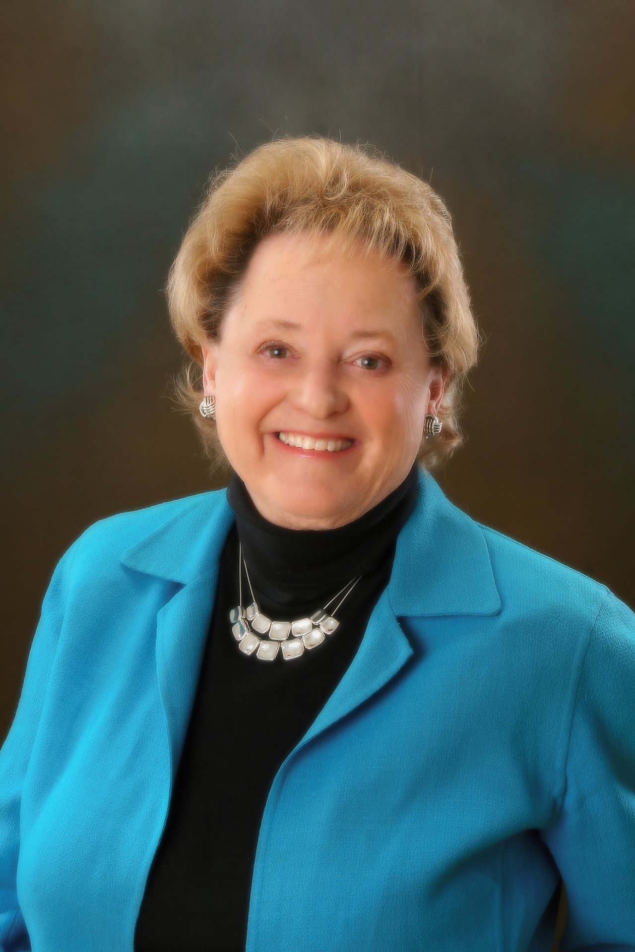 Mary Williams, smiling in a turquoise blazer and silver necklace.