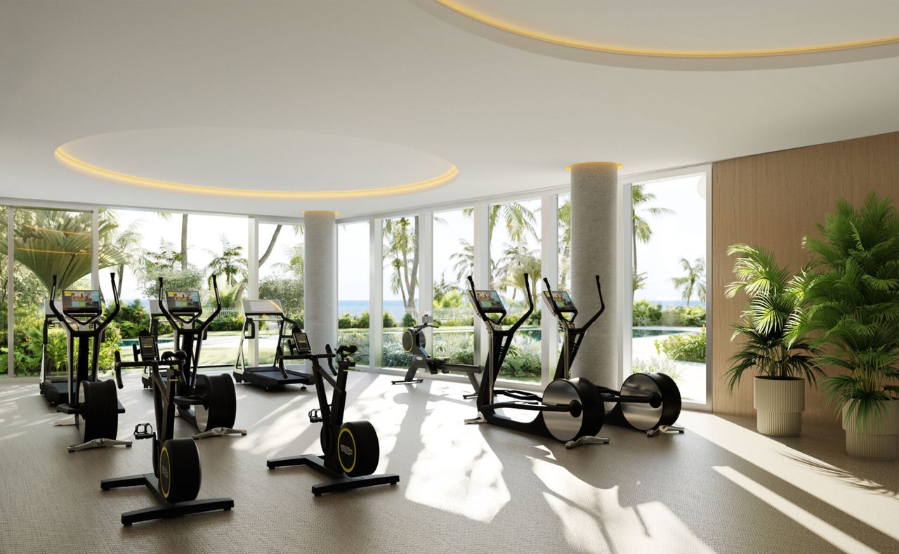 Fitness center with cardio equipment, floor-to-ceiling windows, tropical landscaping, and an ocean view.