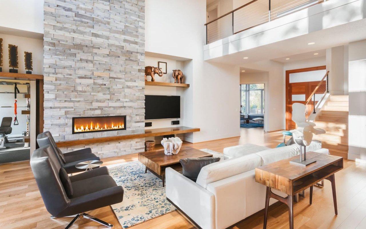 Cozy living room featuring a weathered leather couch, brick fireplace, wooden table, geometric rug, and walkway to gym room.