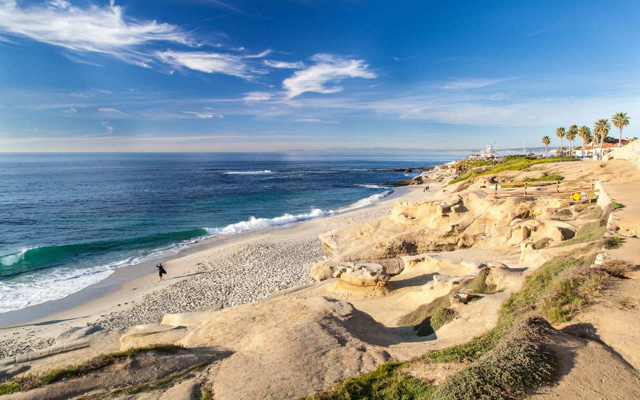 Sunny day at La Jolla sandy beach with blue skies and rolling hills.