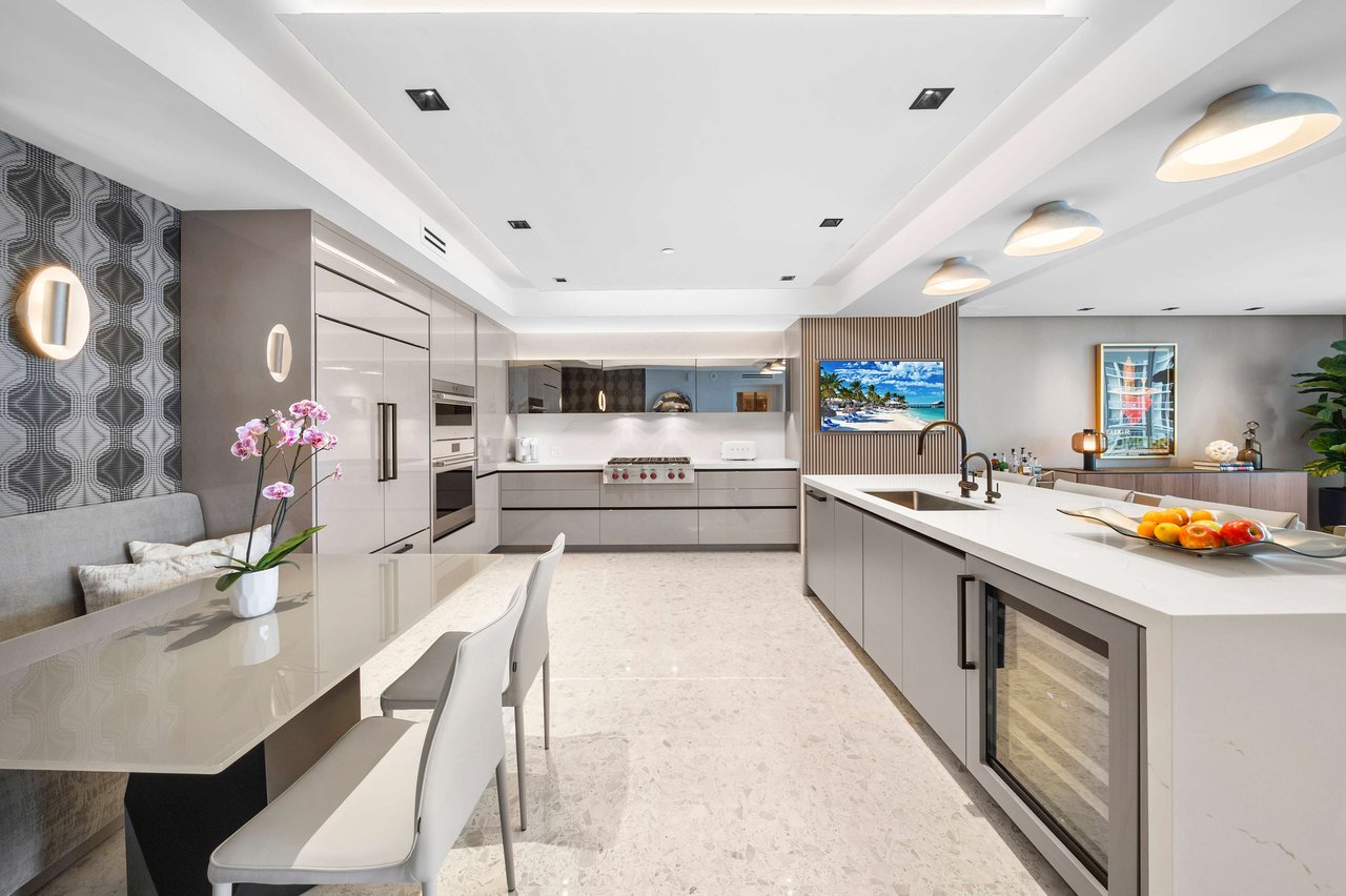 Open kitchen/dining area with gray cabinets, island, bench seating, geometric backsplash, and high-end built-in appliances