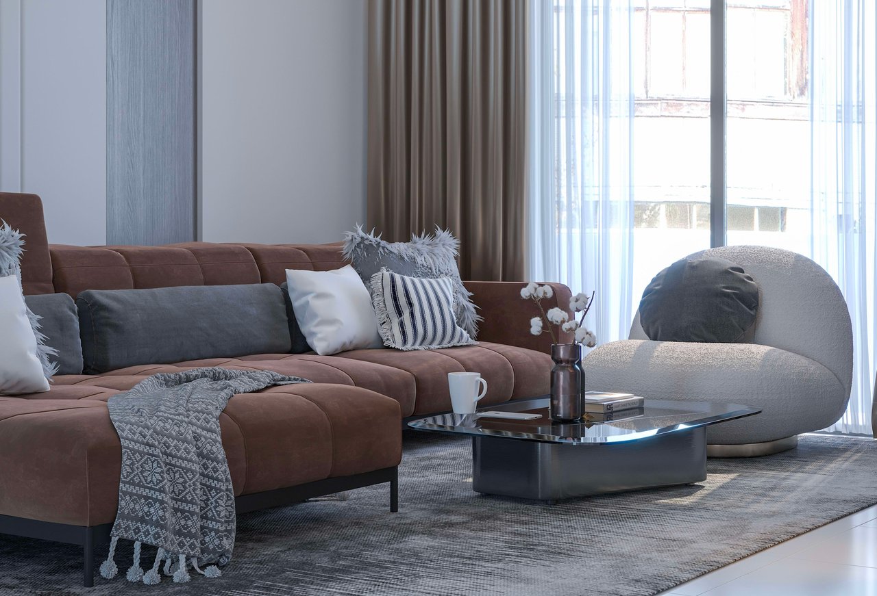 A chic and comfortable living room featuring a large, L-shaped brown sectional sofa adorned with various throw pillows in white, grey, and black stripes, and a grey knitted blanket.