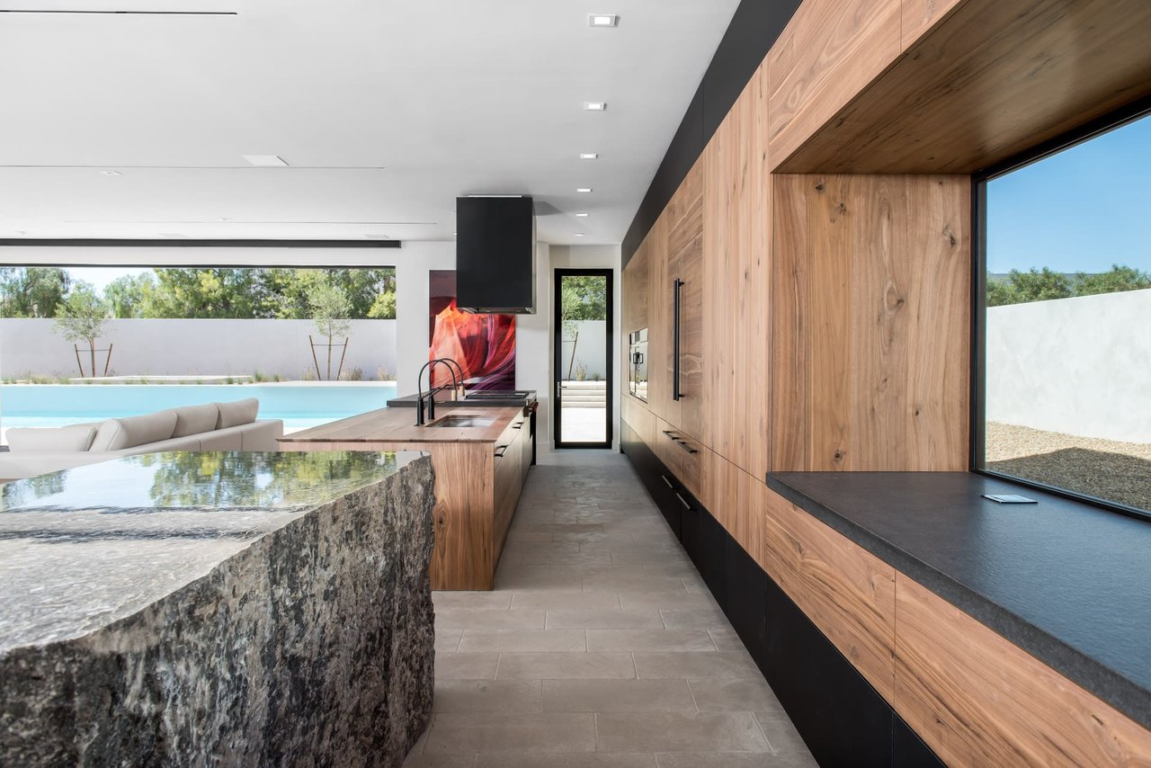 Modern kitchen with warm wood cabinetry, a rough-stone island, and views of a swimming pool.