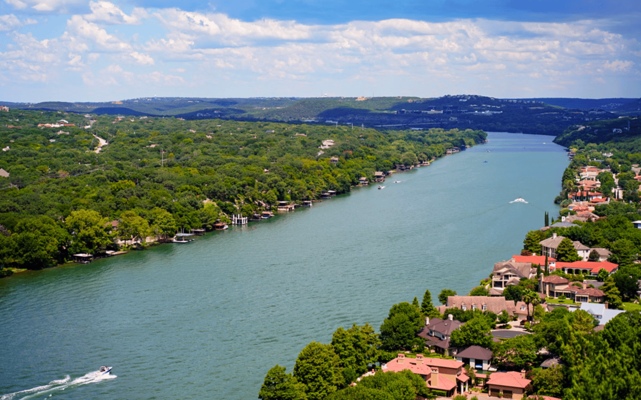 An aerial view of a wide river winding through a hilly landscape with lush greenery and scattered houses along the shore.