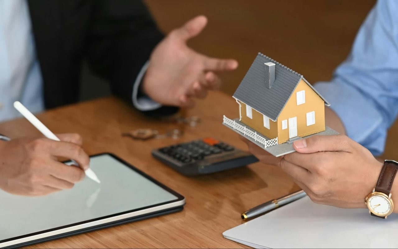 A close-up shot of two people engaged in a business transaction, likely a real estate deal, as one person holds a small model house.