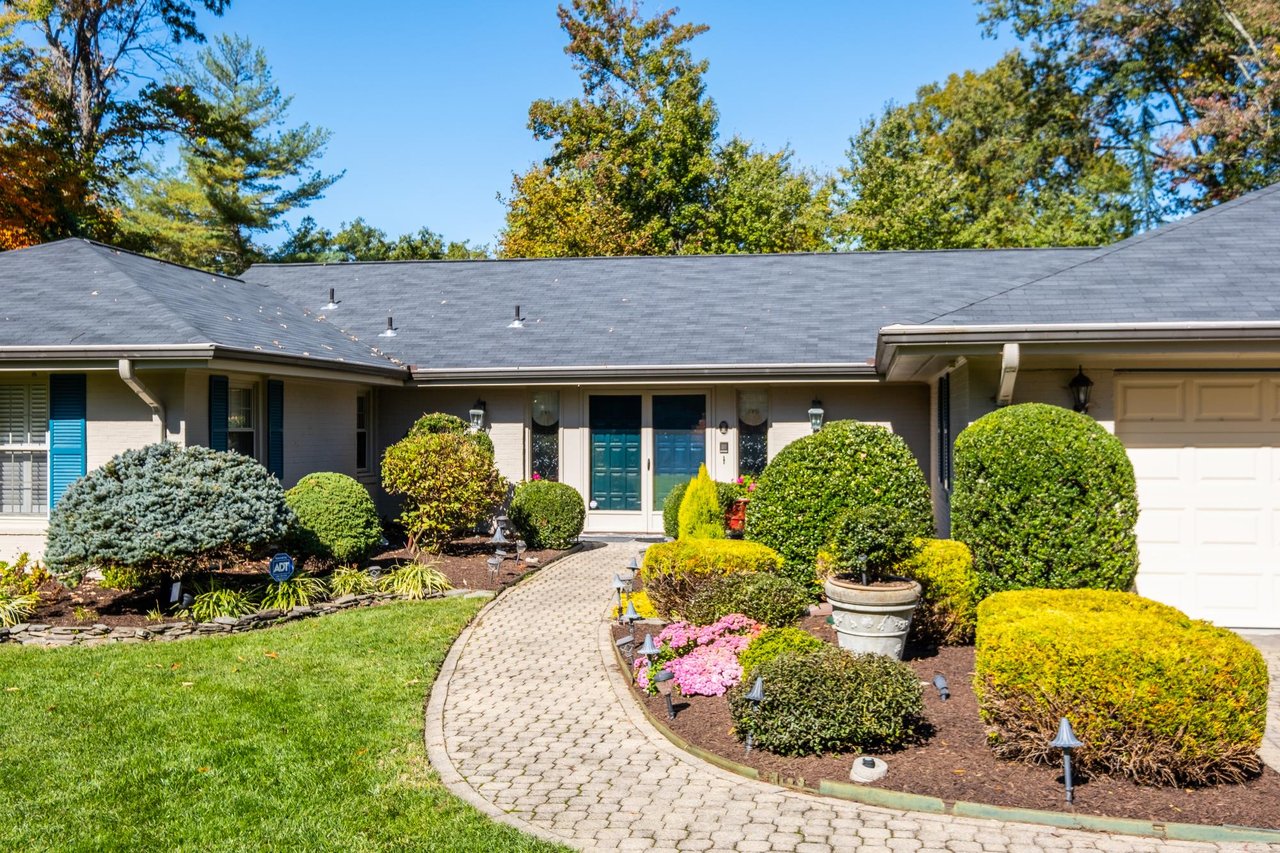 Single-story brick home with teal front door, attached garage, and a curved walkway through landscaped gardens.