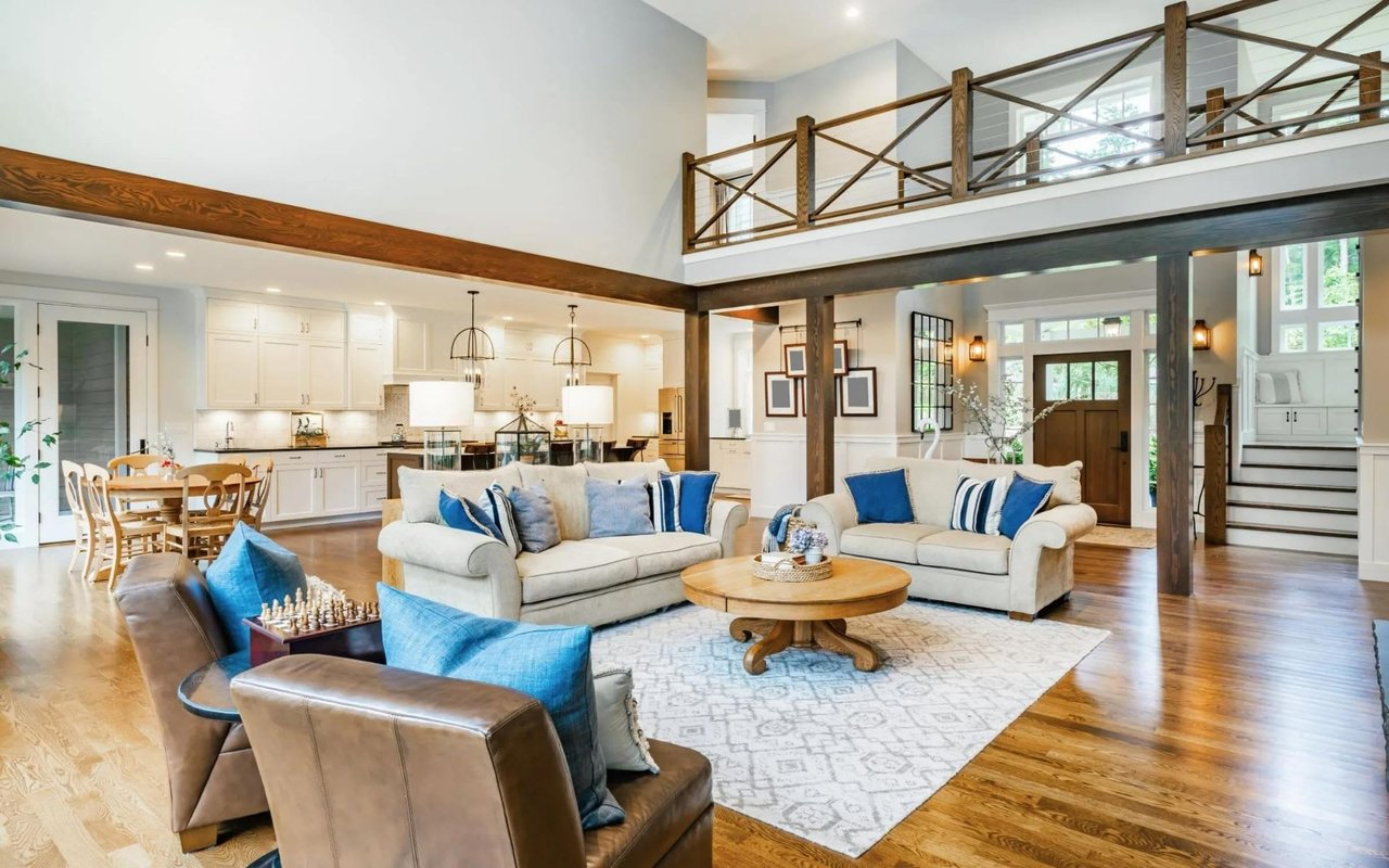 Open-plan living room and kitchen with hardwood floors, exposed beams, and a mezzanine balcony.