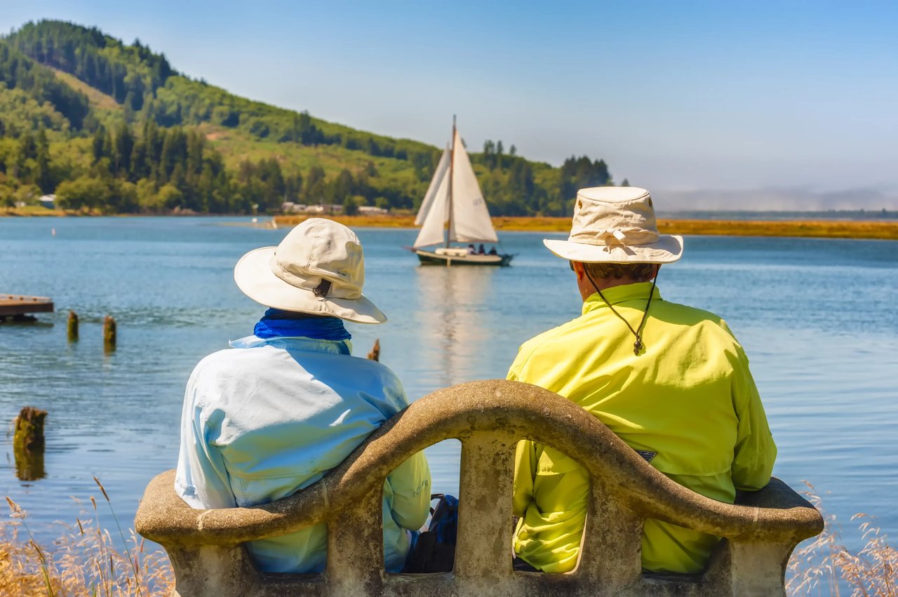 old couple watch a sailboat in neahlem bay from the wheeler oregon park bench