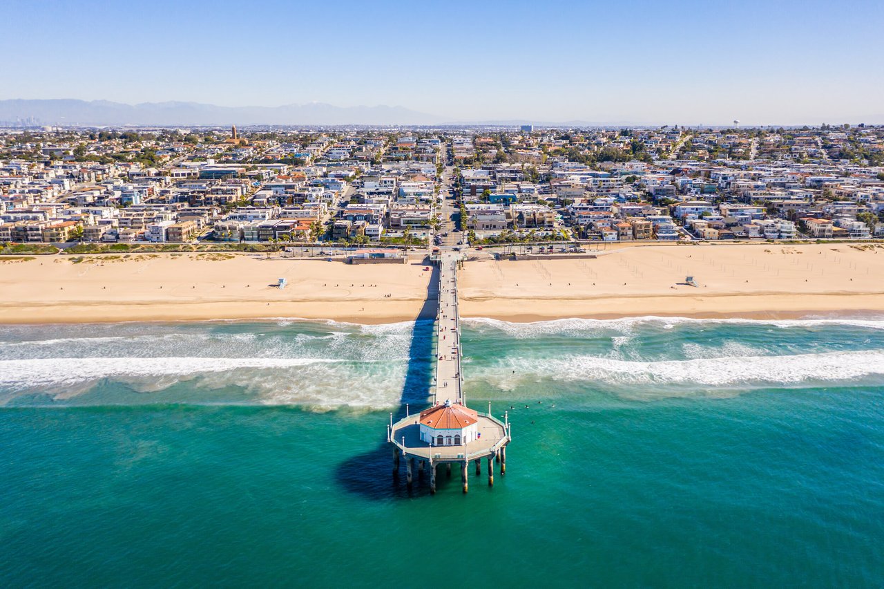 The pier stretches into the turquoise ocean, beach town below, and mountains in the distance.