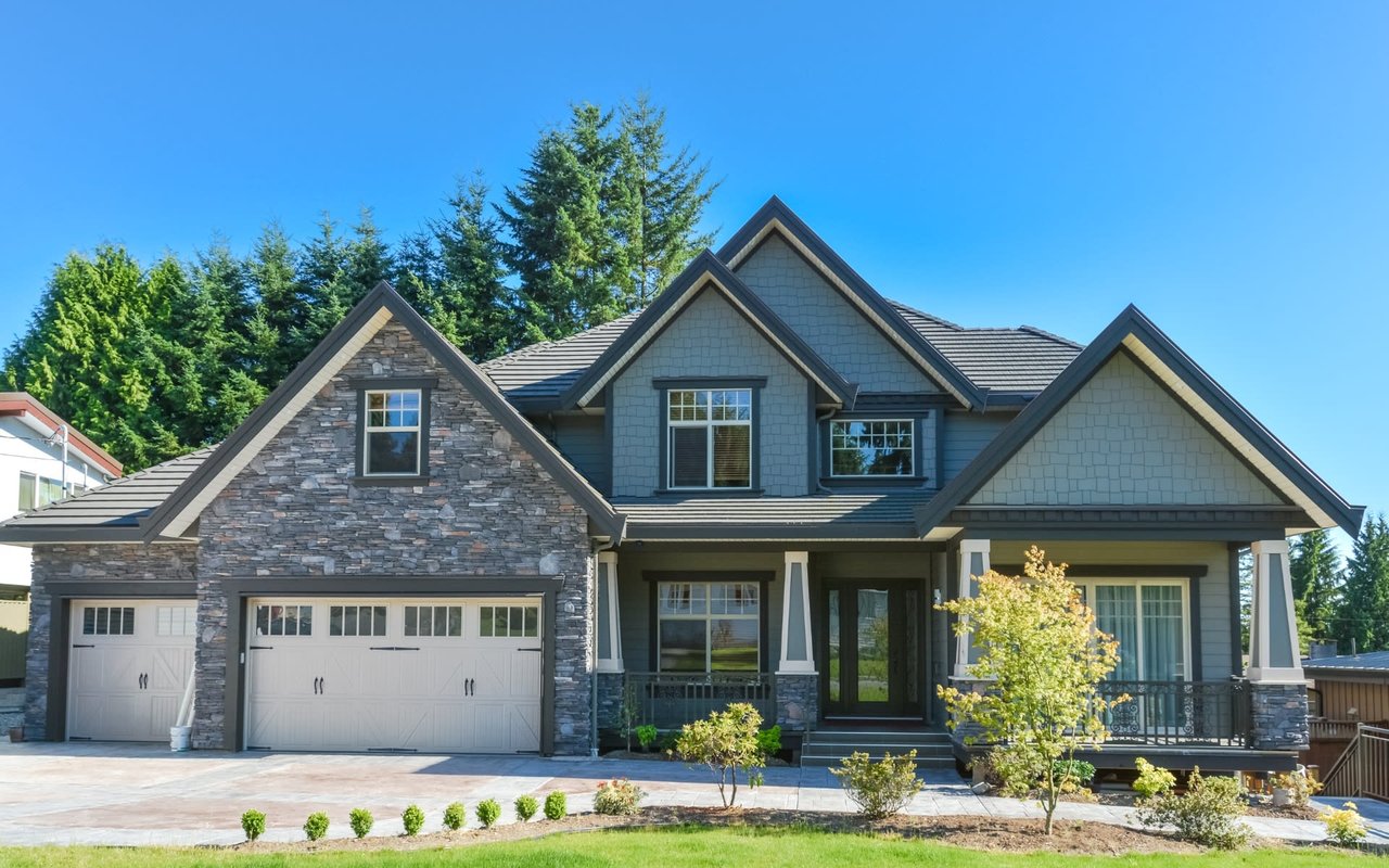 The house is surrounded by green grass and trees, and there is a blue sky in the background. 