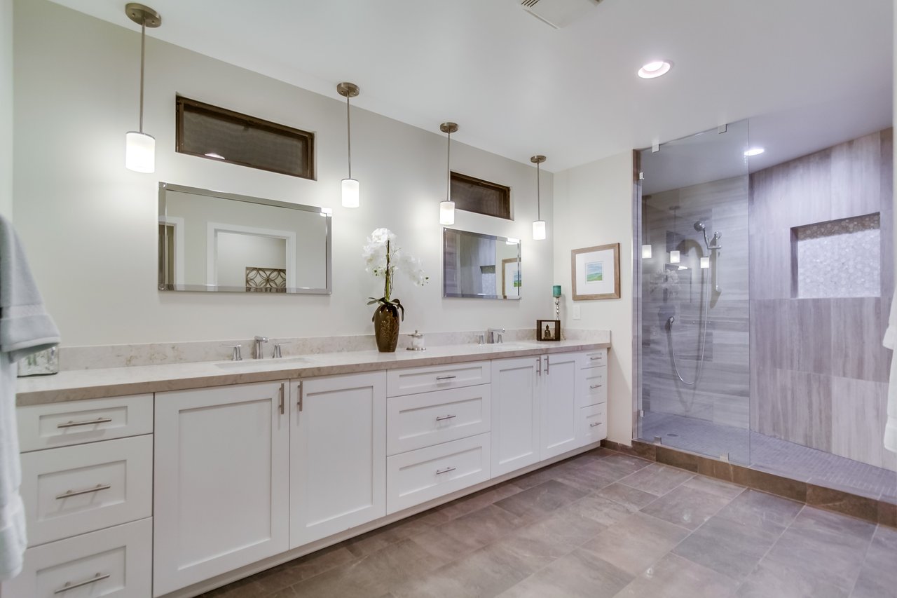 Bathroom with a long white double vanity and a glass-enclosed gray-tile shower.