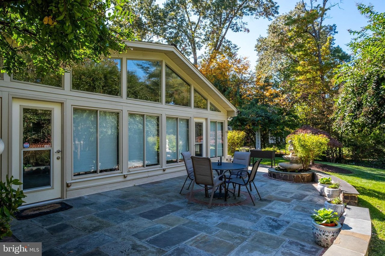 Home exterior with a broad-windowed facade, stone patio furniture, and a landscaped garden fountain.