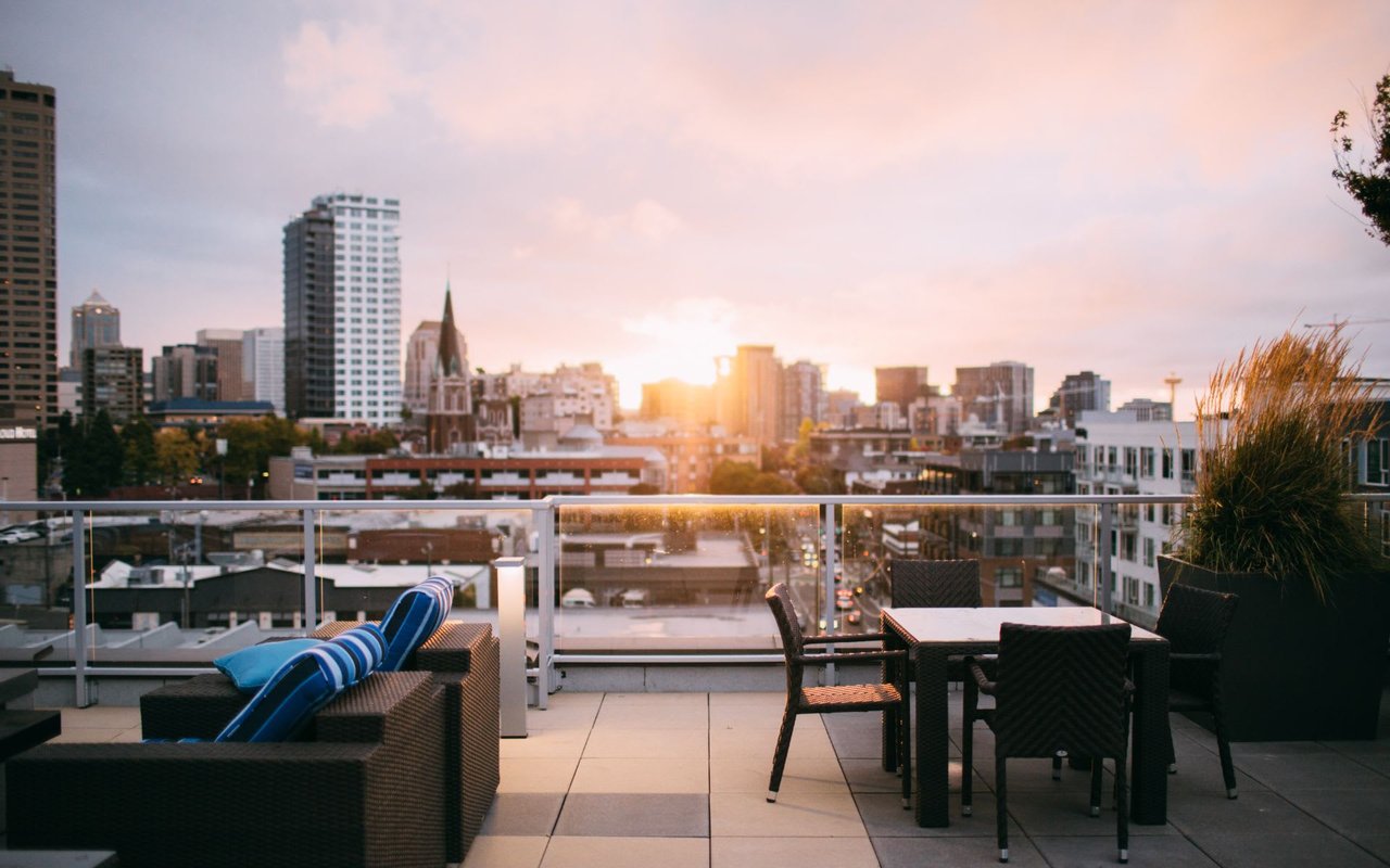  A rooftop patio with lounge seating and a dining table, overlooking a city skyline at sunset.