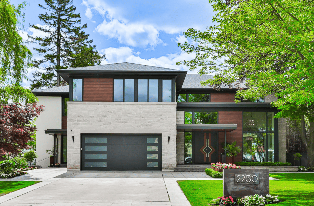 Large modern house with 3-car garage, floor-to-ceiling windows, and balcony overlooking wooded area