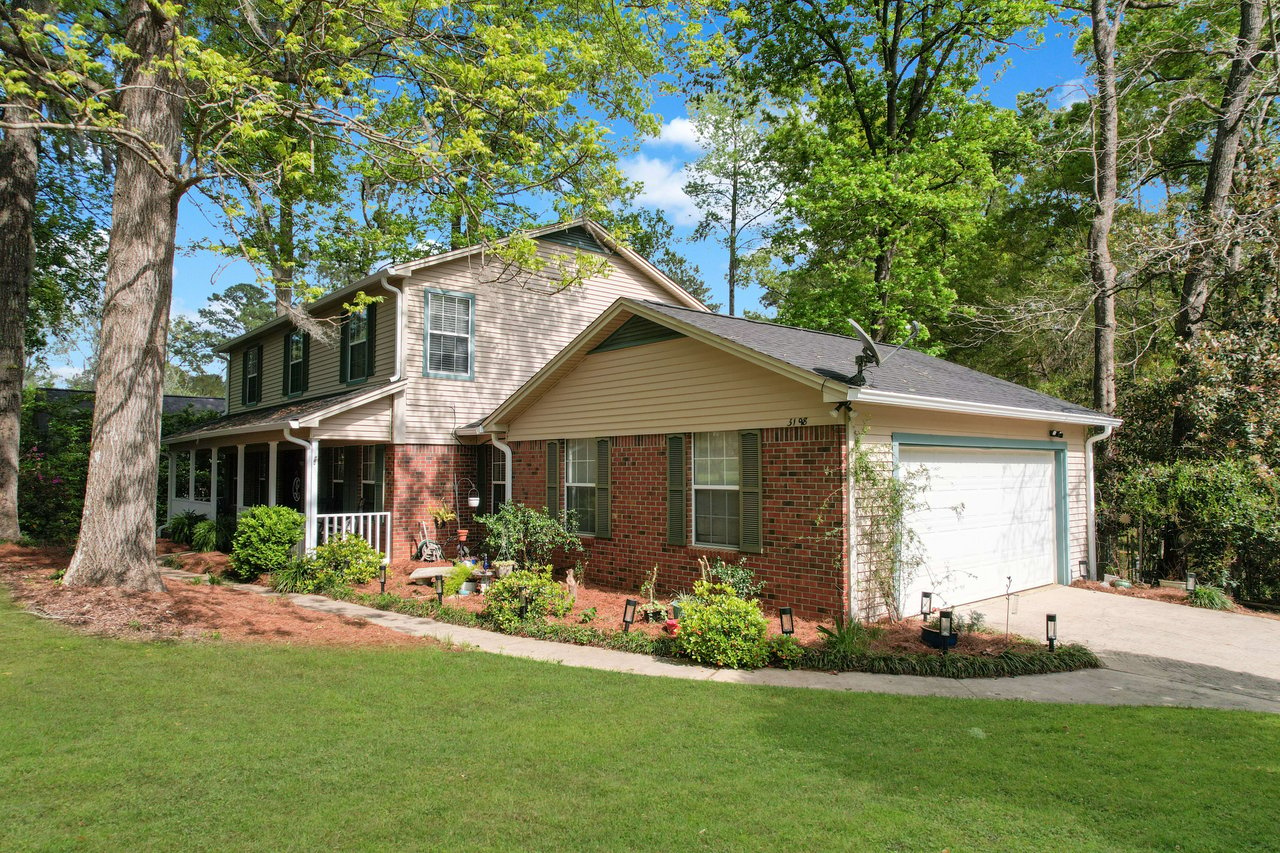 An exterior view of a house with a well-maintained lawn. The house features a brick and siding exterior, a two-story design, and is surrounded by trees and landscaping.