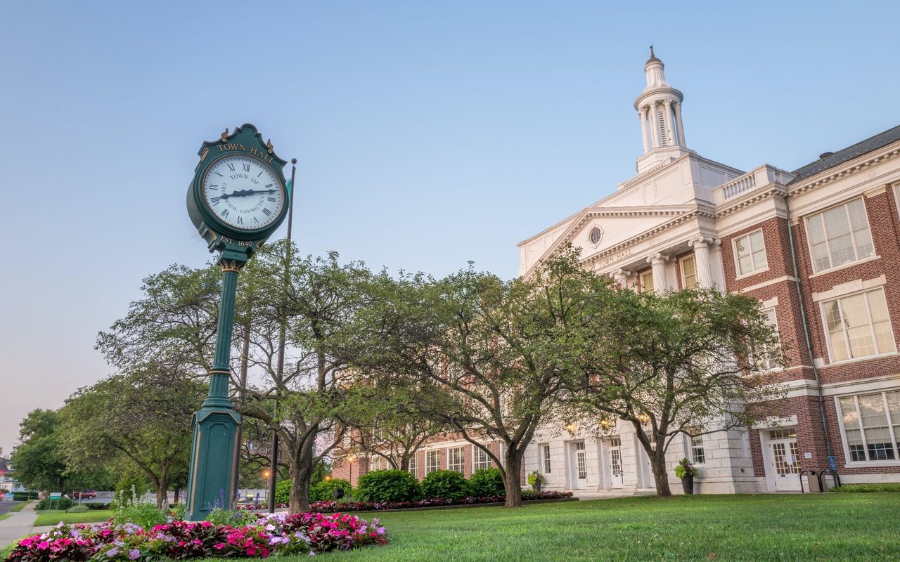 front of the building, with a clock tower and a large lawn in the foreground