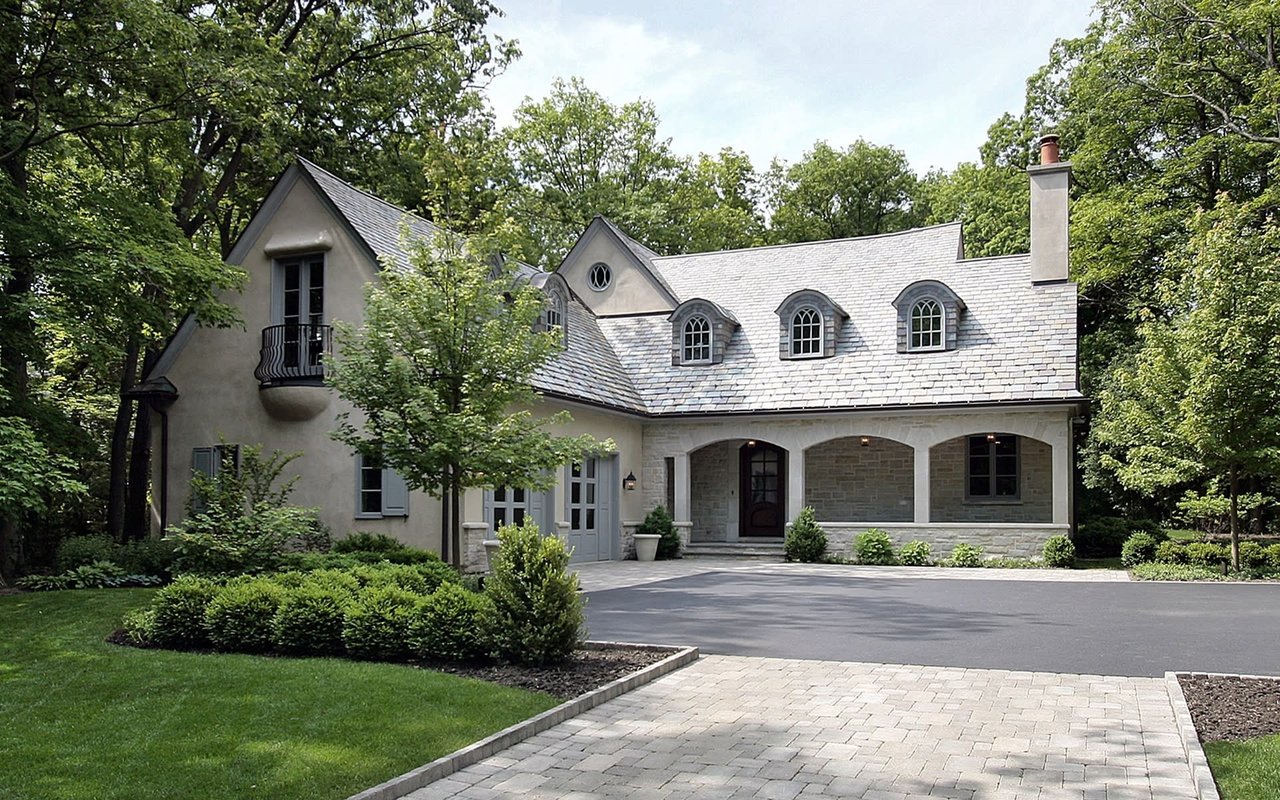 A large, two-story white house with a black shingle roof, chimney, covered porch, front lawn, and asphalt driveway.