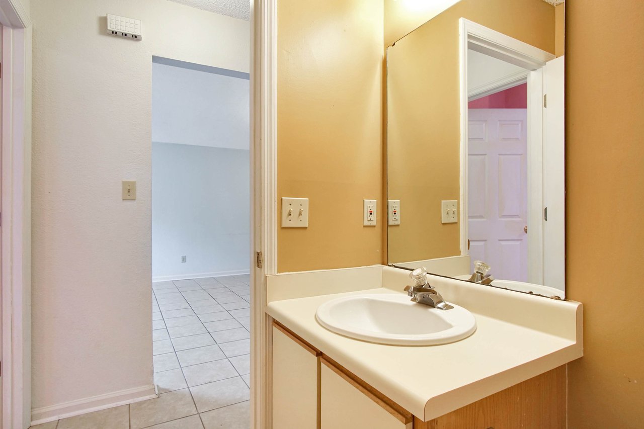 Photo of guest bathroom featuring yellow walls, a vanity light fixture, a large mirror, a vanity with white sink, lightly wood colored cabinets, and overlooking the main living area  at 2709 Oak Park Court, Tallahassee, Florida 32308