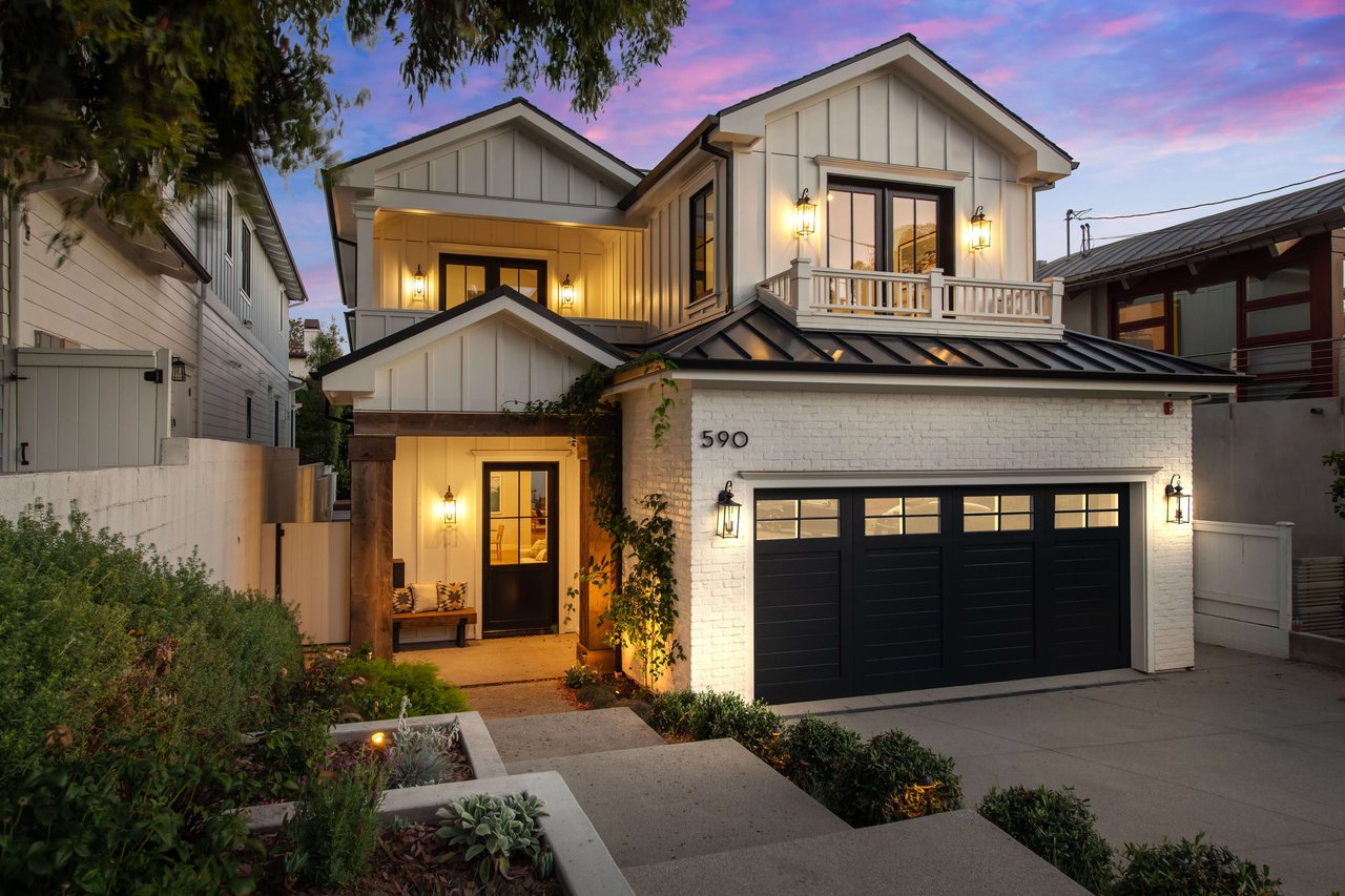 A modern farmhouse with a white exterior, black accents, and a metal roof sits on a landscaped lot.