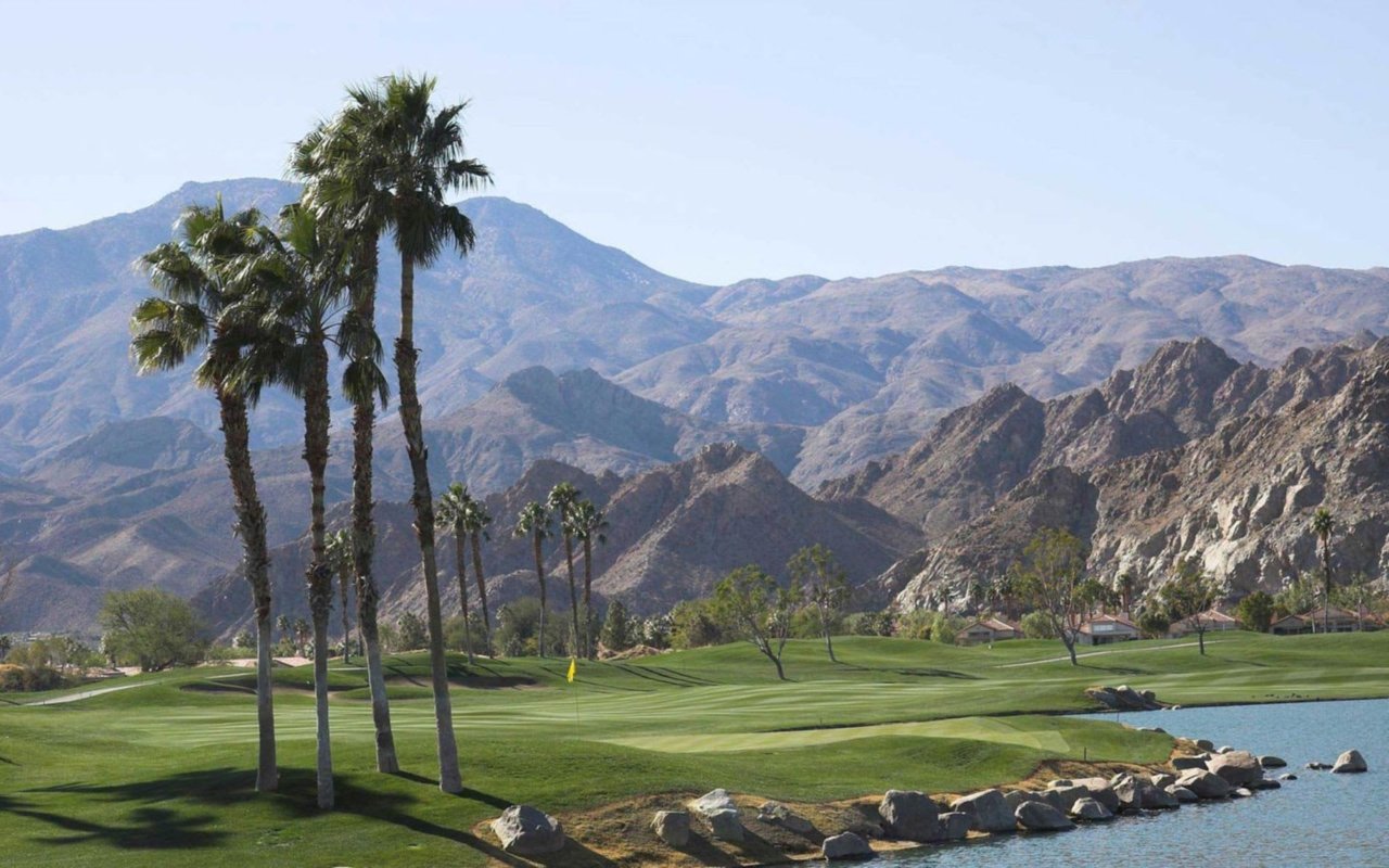 Golf course with palm trees, a pond and rugged mountains in the background.