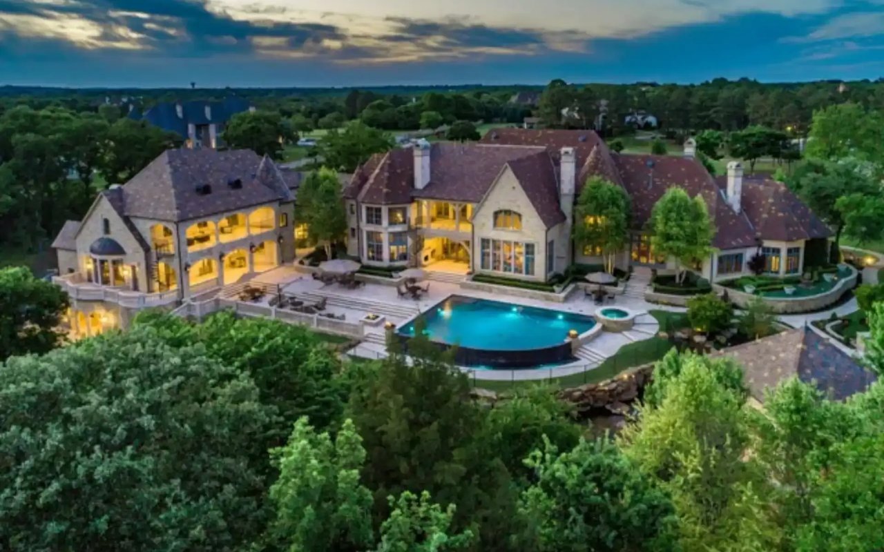 An aerial view of a large, two-story mansion, swimming pool, patio, and backyard at Chateau Du Lac in Flower Mound, Texas.