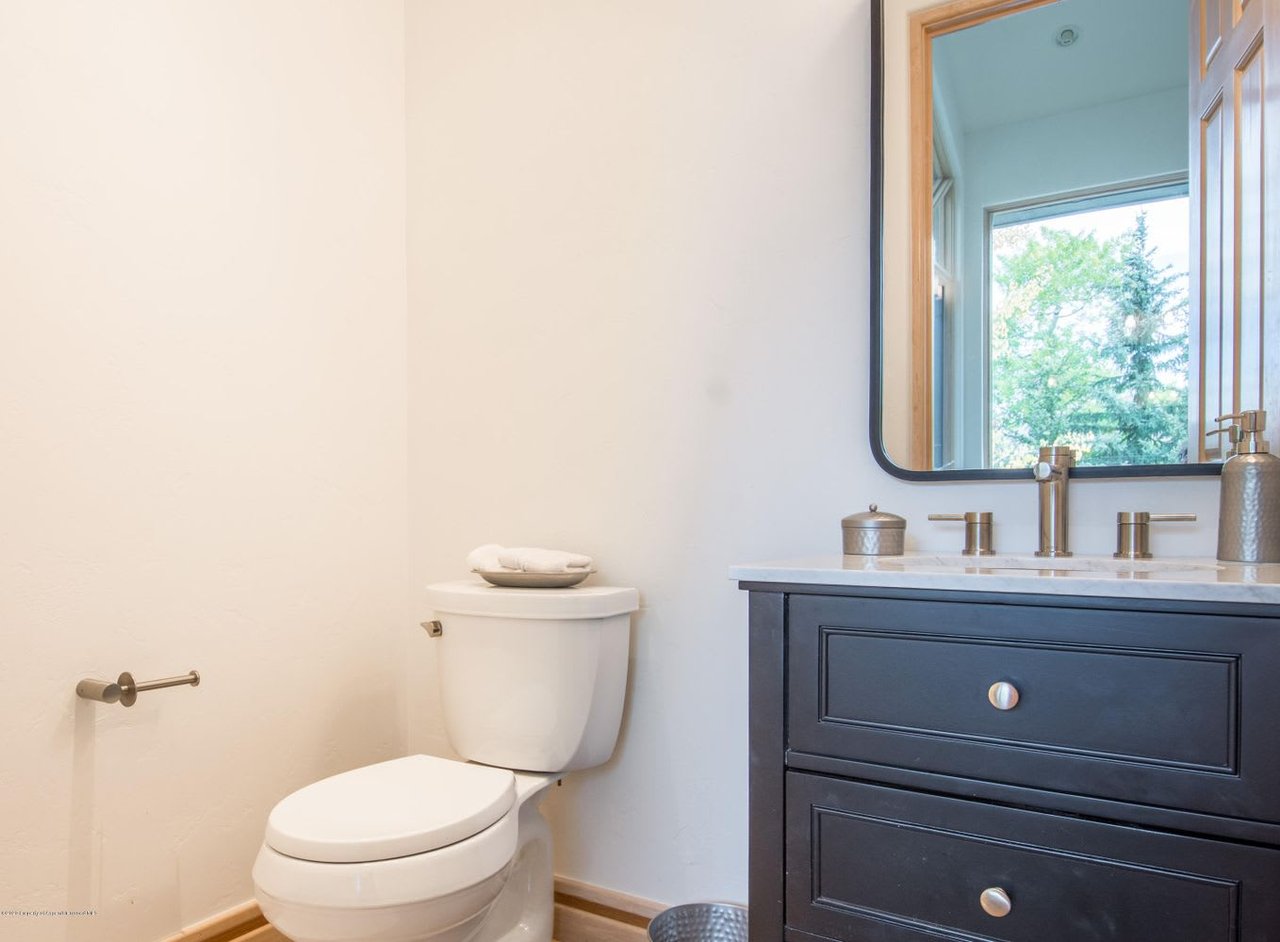 Bathroom with a dark blue vanity, marble countertop, and large mirror reflecting trees through a window.
