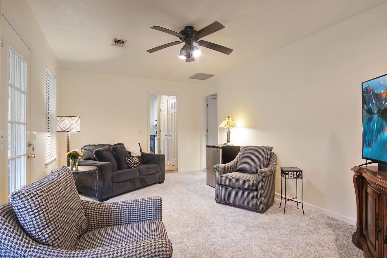 The room has comfortable seating, a ceiling fan, and large windows, providing a bright and airy atmosphere.