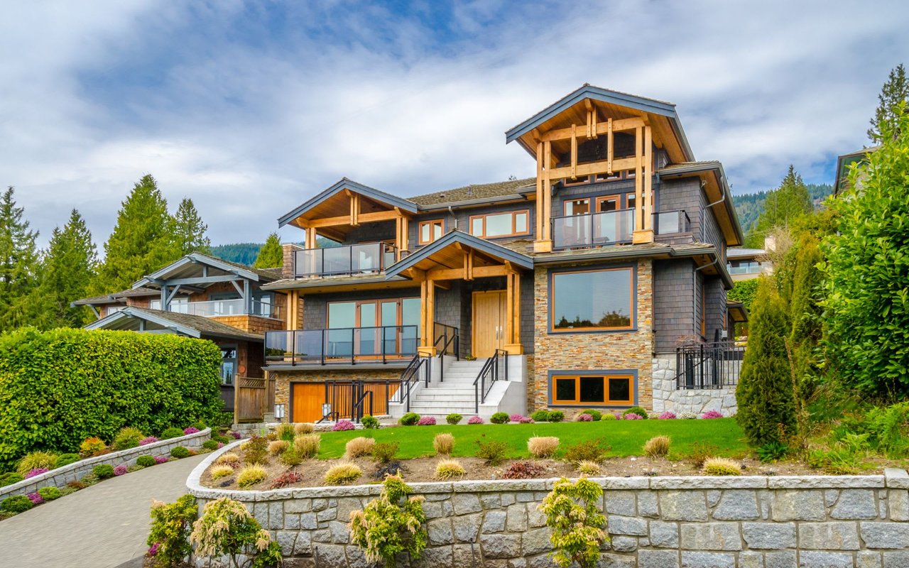 A modern mansion with floor-to-ceiling windows sits on a rocky cliff overlooking the environment.