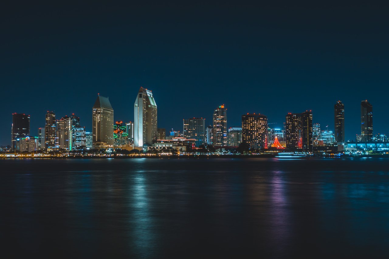 San Diego skyline glowing across the harbor at night, with lights reflected on the water.