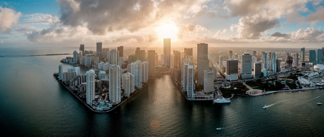 Miami waterfront skyline seen from above, with the river and bay reflecting the setting sun.