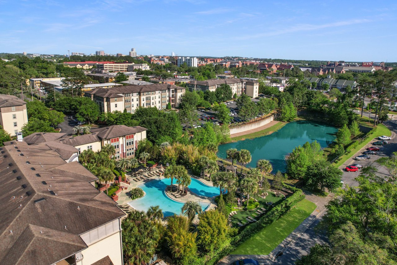 An aerial view of the Campus Circle community, featuring residential buildings around a central water body with lush greenery and recreational areas.