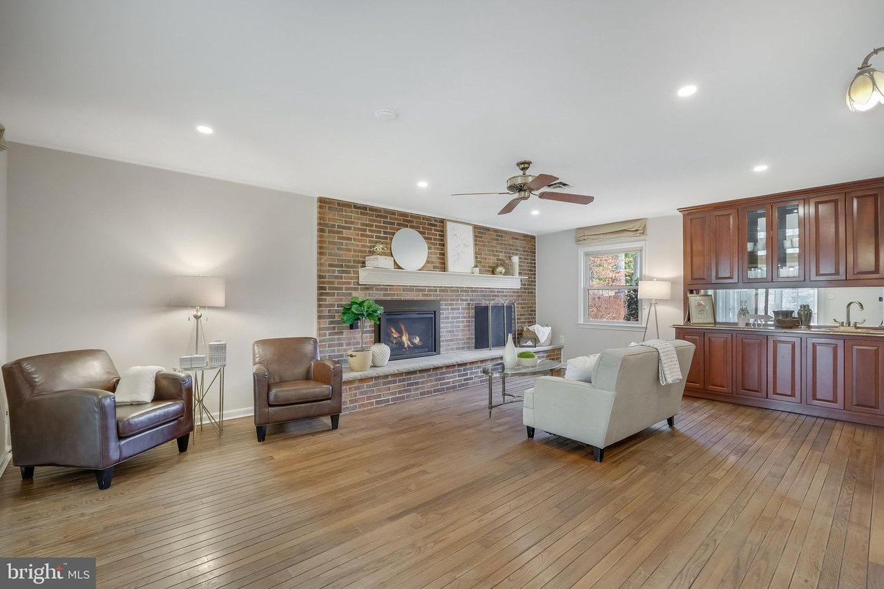 Living room with a brick fireplace, leather armchairs, hardwood floors, and built-in wet bar.