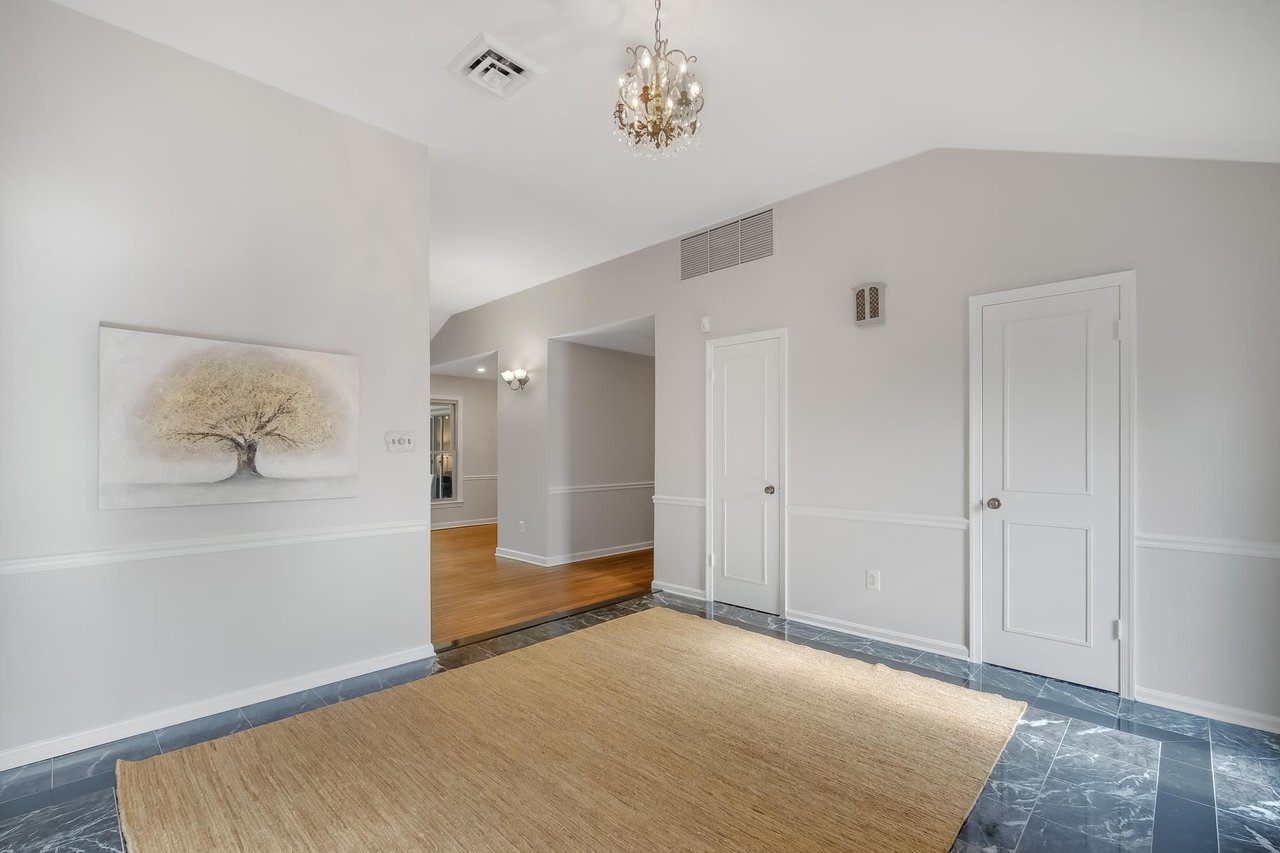 Entry foyer with dark marble tile, a large tan rug, chandelier, and hardwood hallway.