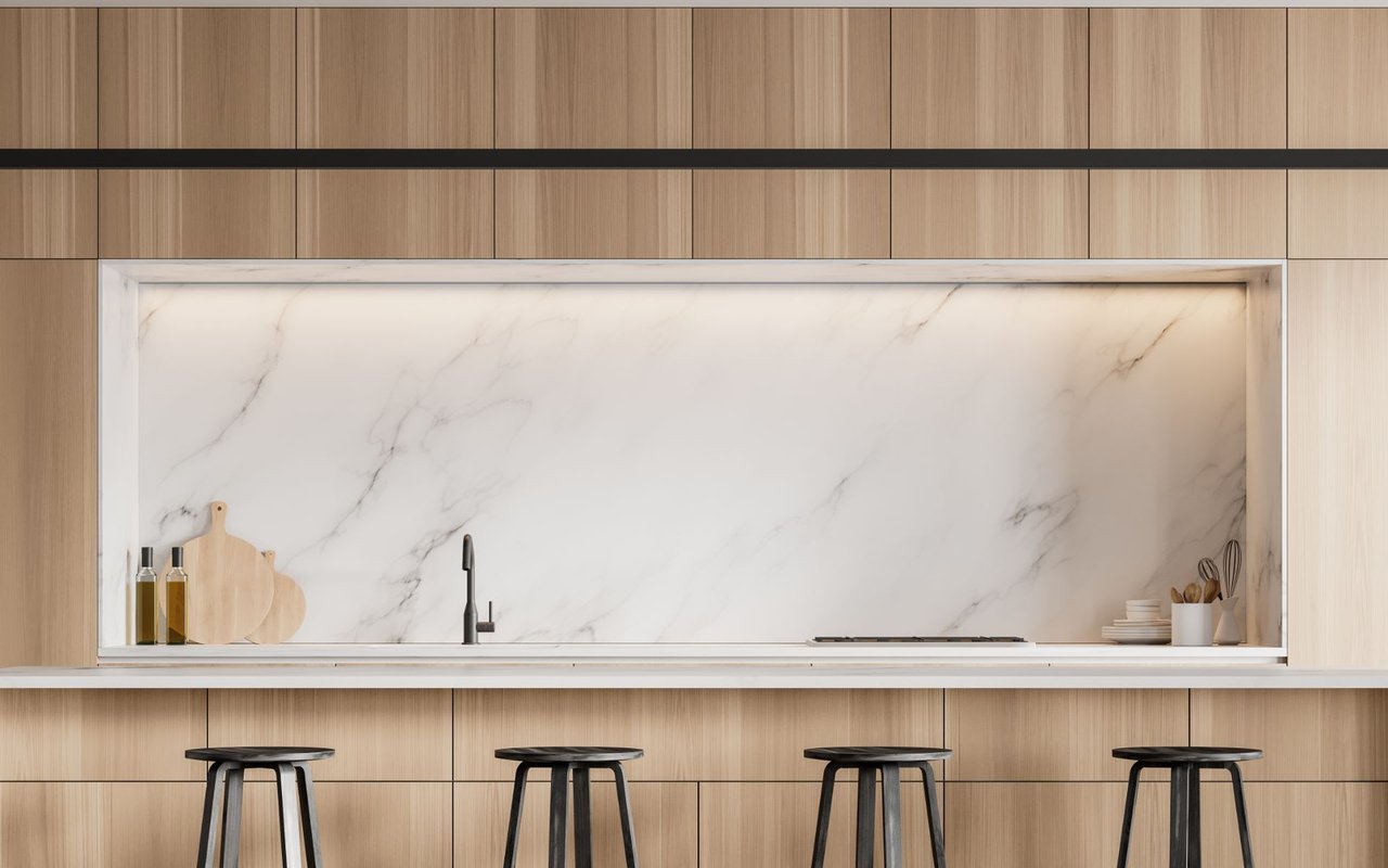 A kitchen with a marble countertop, wooden cabinets, kitchen utensils, and metal bar stools.