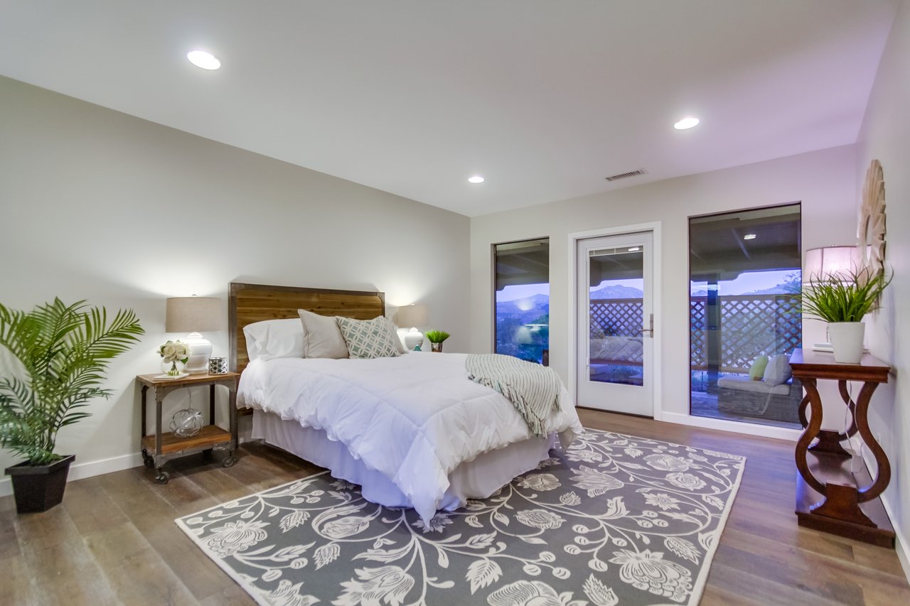 Staged bedroom with a white bed, patterned rug, and glass doors overlooking mountains.