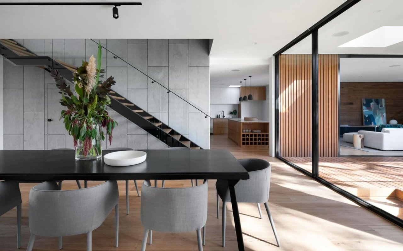 Modern dining room with gray chairs, black table, and large floral arrangement, leading to an open kitchen and living area.