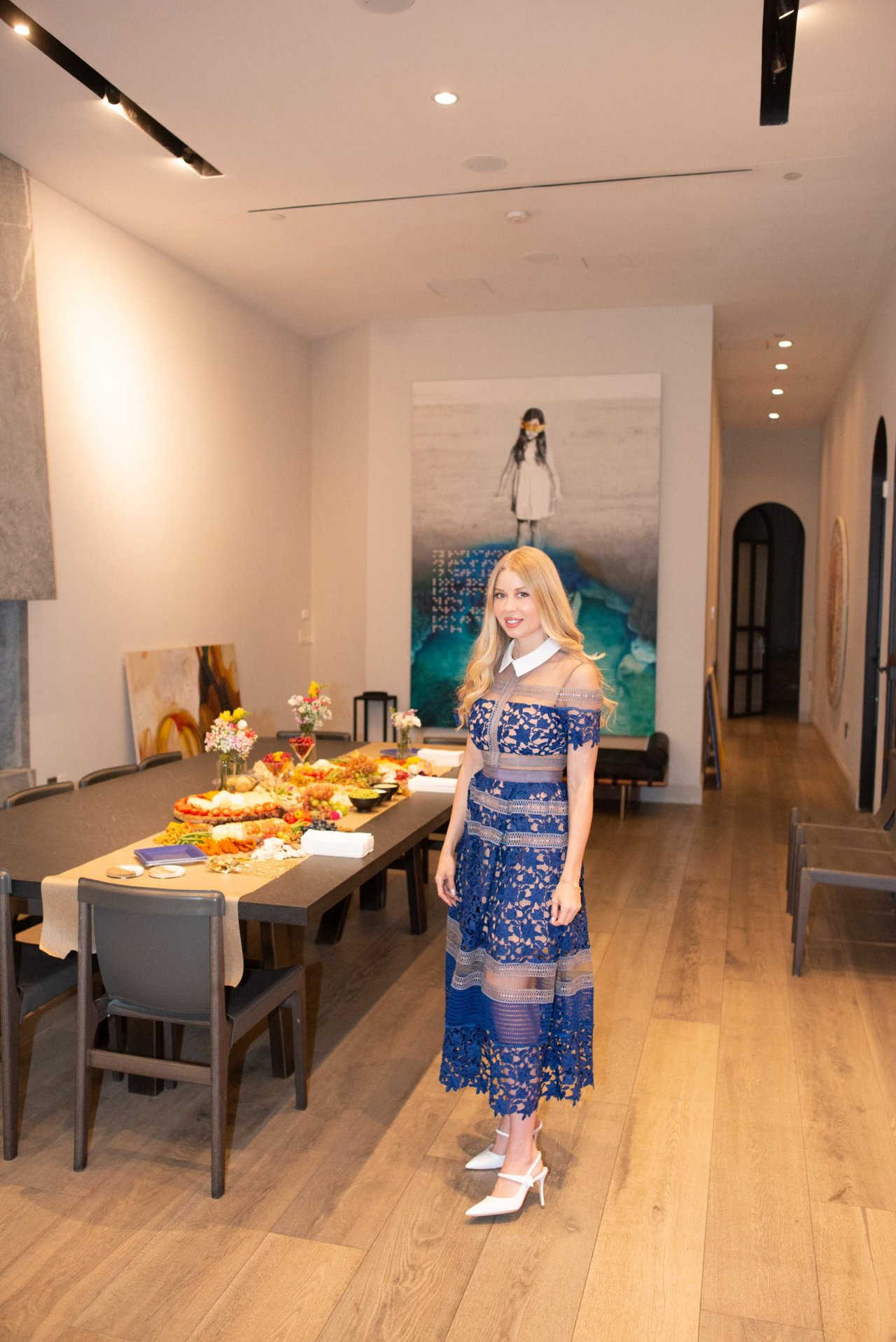 Woman in a blue lace dress beside a buffet table in a modern dining room.