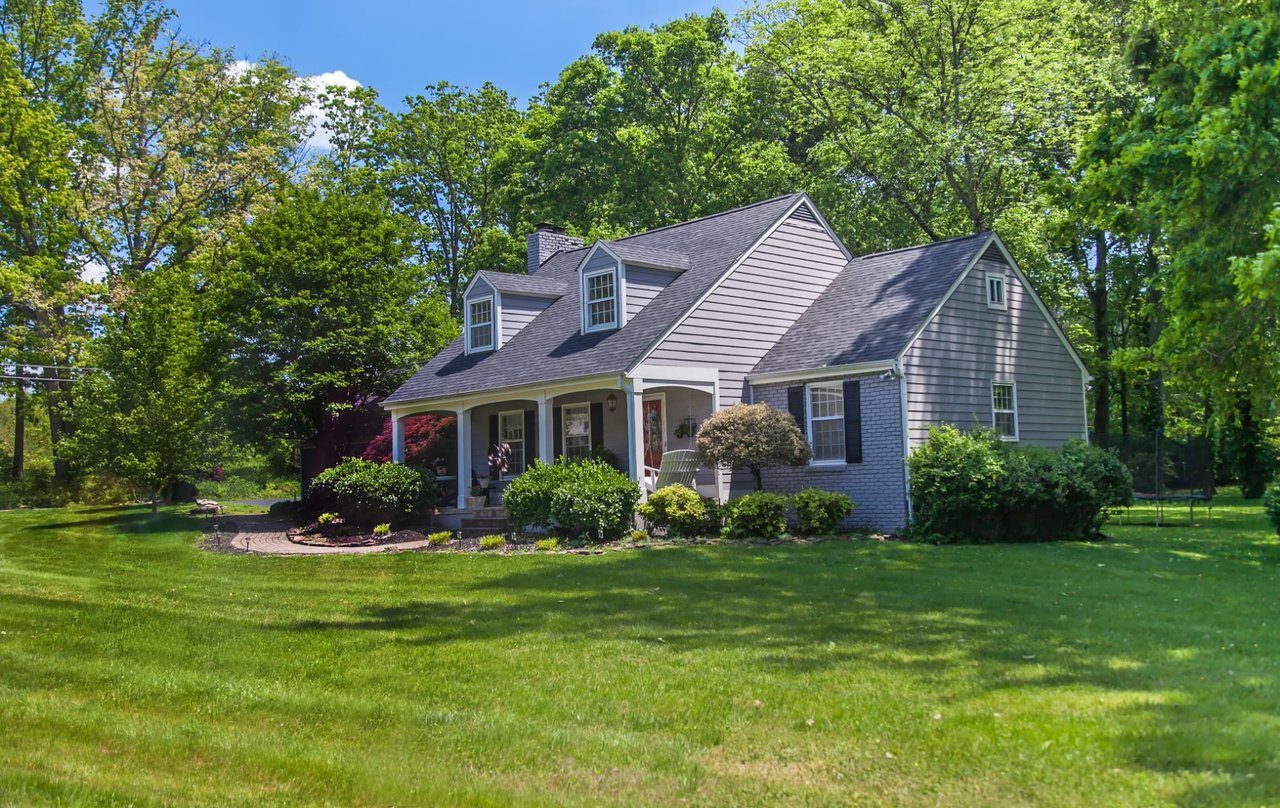 A house with a large grassy lawn in front and surrounded by mature trees with full green foliage.