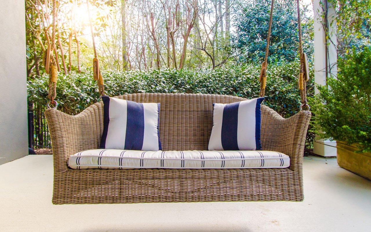 A wicker porch swing hanging from a rope on a porch