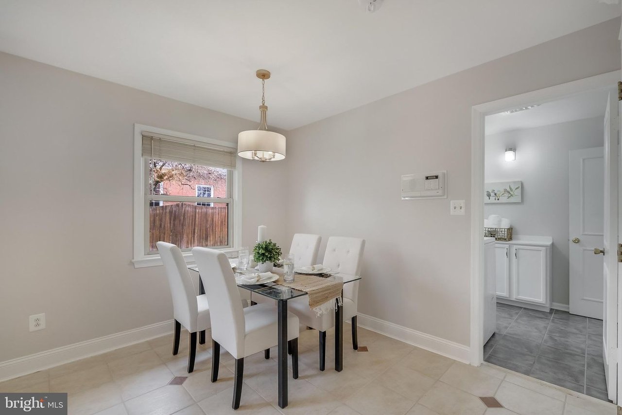 Dining room with a glass-top table, white chairs, and an open doorway to a tiled room.