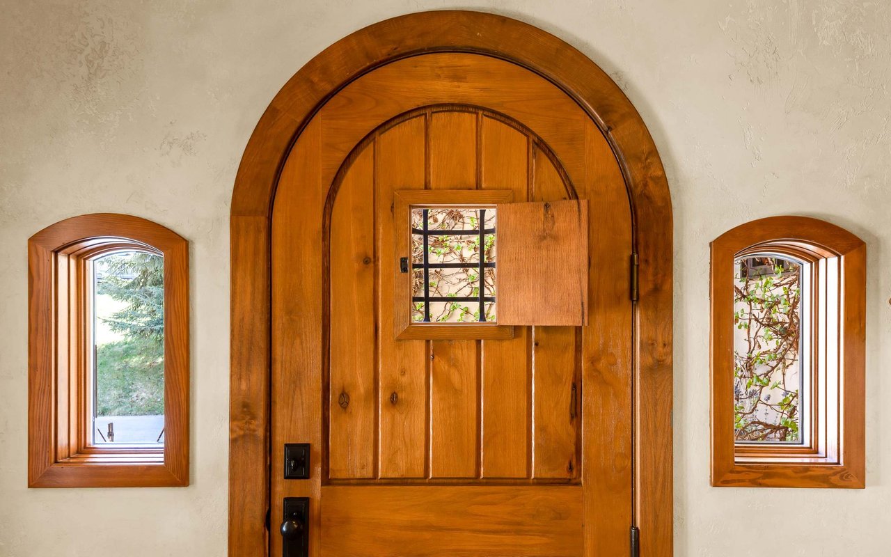 Arched solid wood door with peephole flanked by two small wood-wrapped windows.