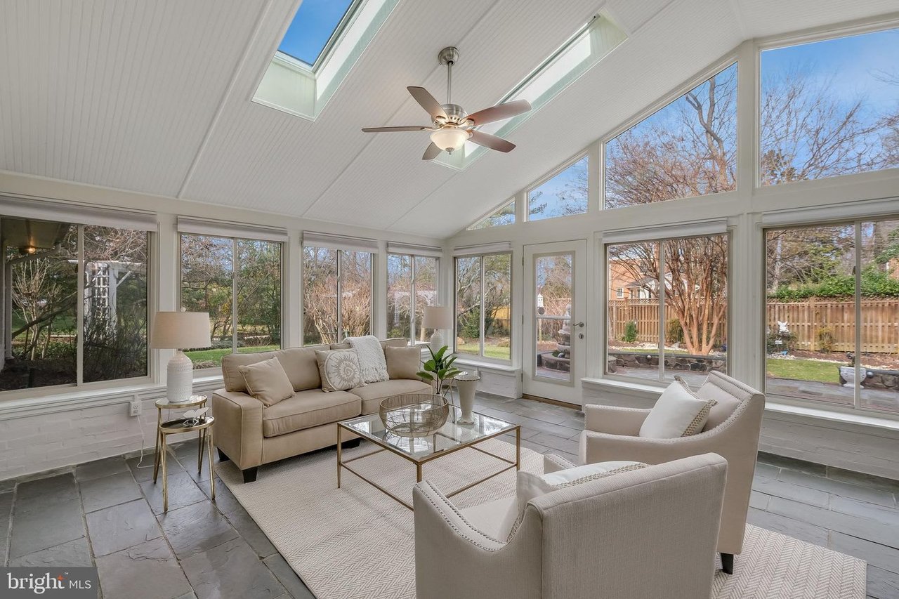 Furnished sunroom with skylights, large garden-facing windows, and a sofa with two armchairs.