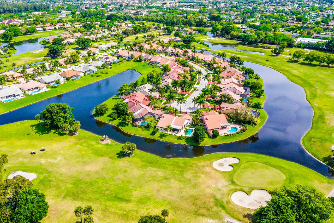 Houses bathed in sunlight, surrounded by lush greenery, form a colorful quilt under a clear sky.