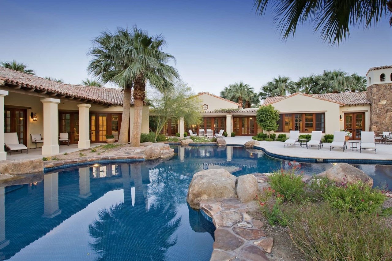 Luxurious backyard with a large pool, palm trees, and a Mediterranean-style home with terracotta roof.