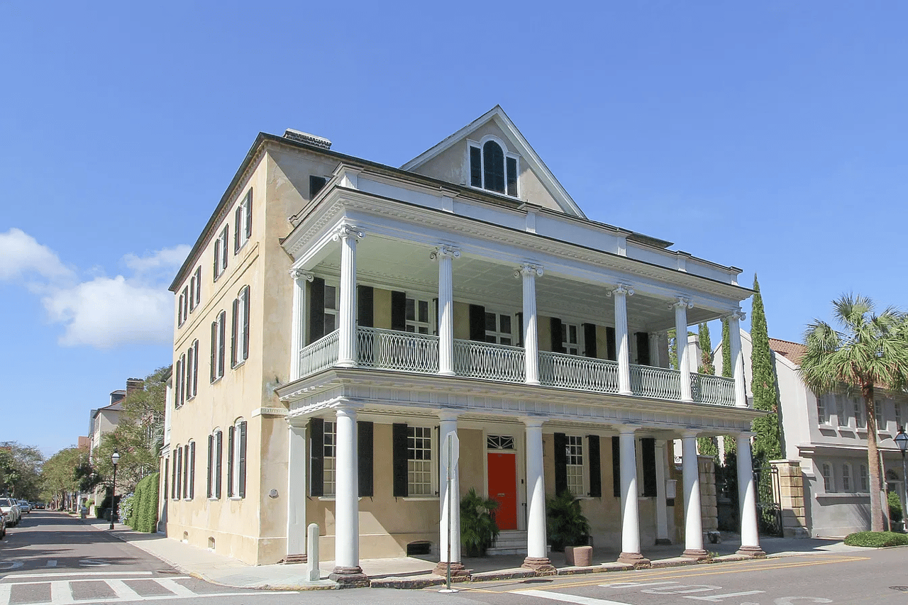 Historic house with a two-story columned porch, black shutters, and a red front door.