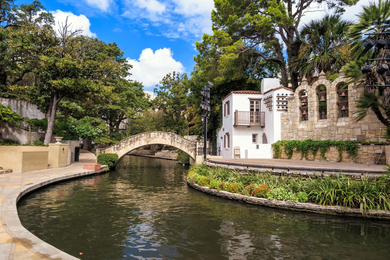 The image shows a stone arch bridge over a river with a white house on one side.